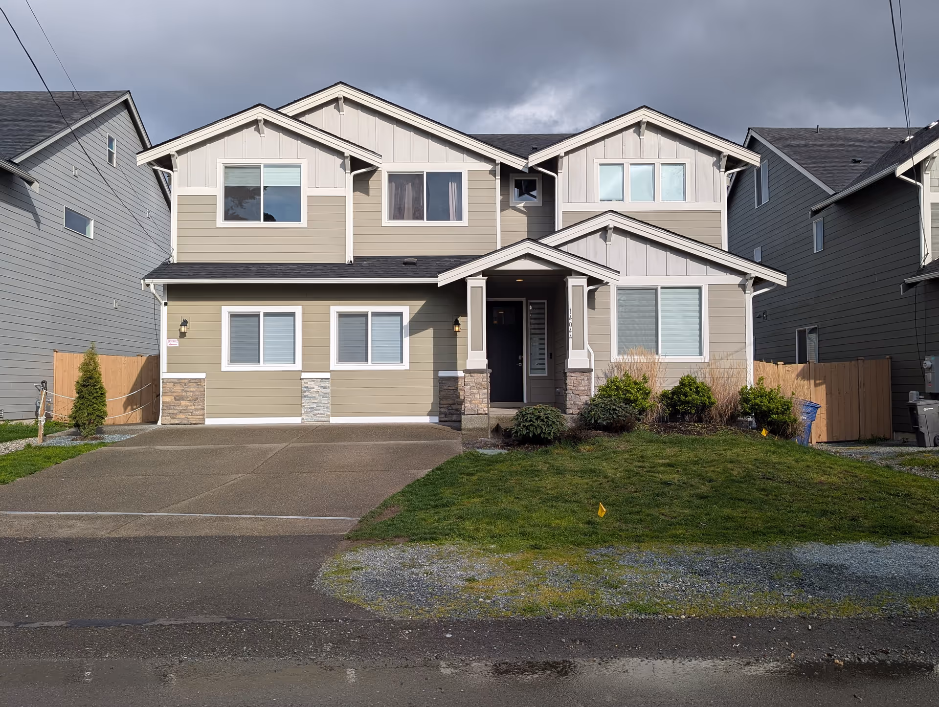 Front view of a two-story beige residential building with a covered entrance and shrubs.