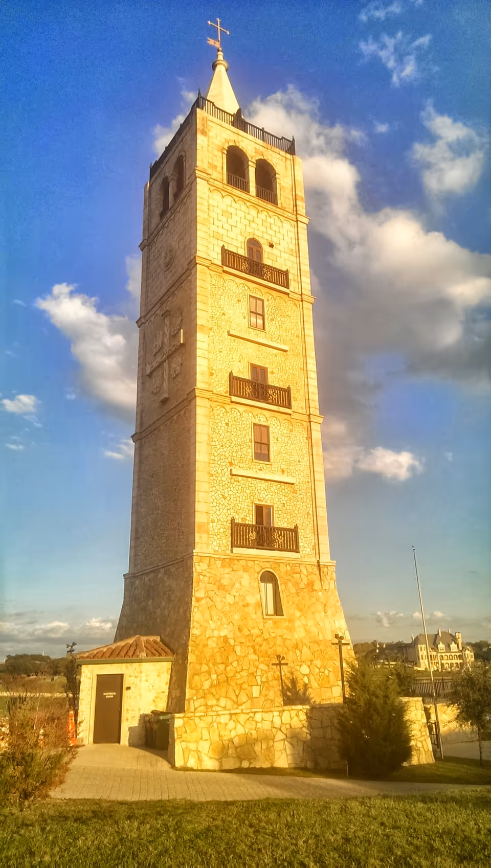 Tall stone tower with arched windows and a cross atop, set against a blue sky.