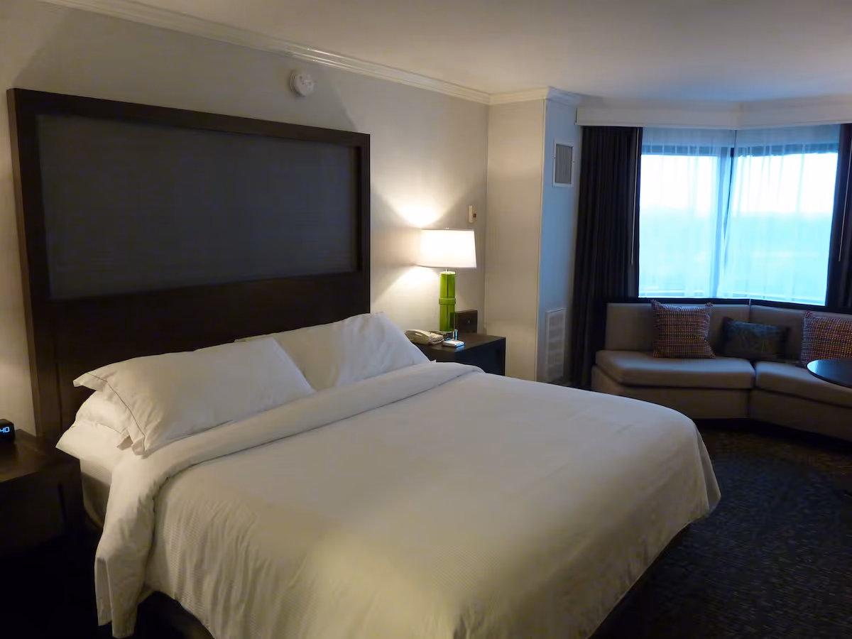 Hotel-style bedroom with a large bed and a sitting area by the window.