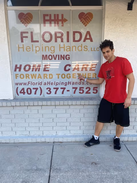 A man in a red shirt stands outside a storefront with 'Florida Helping Hands, LLC' sign.