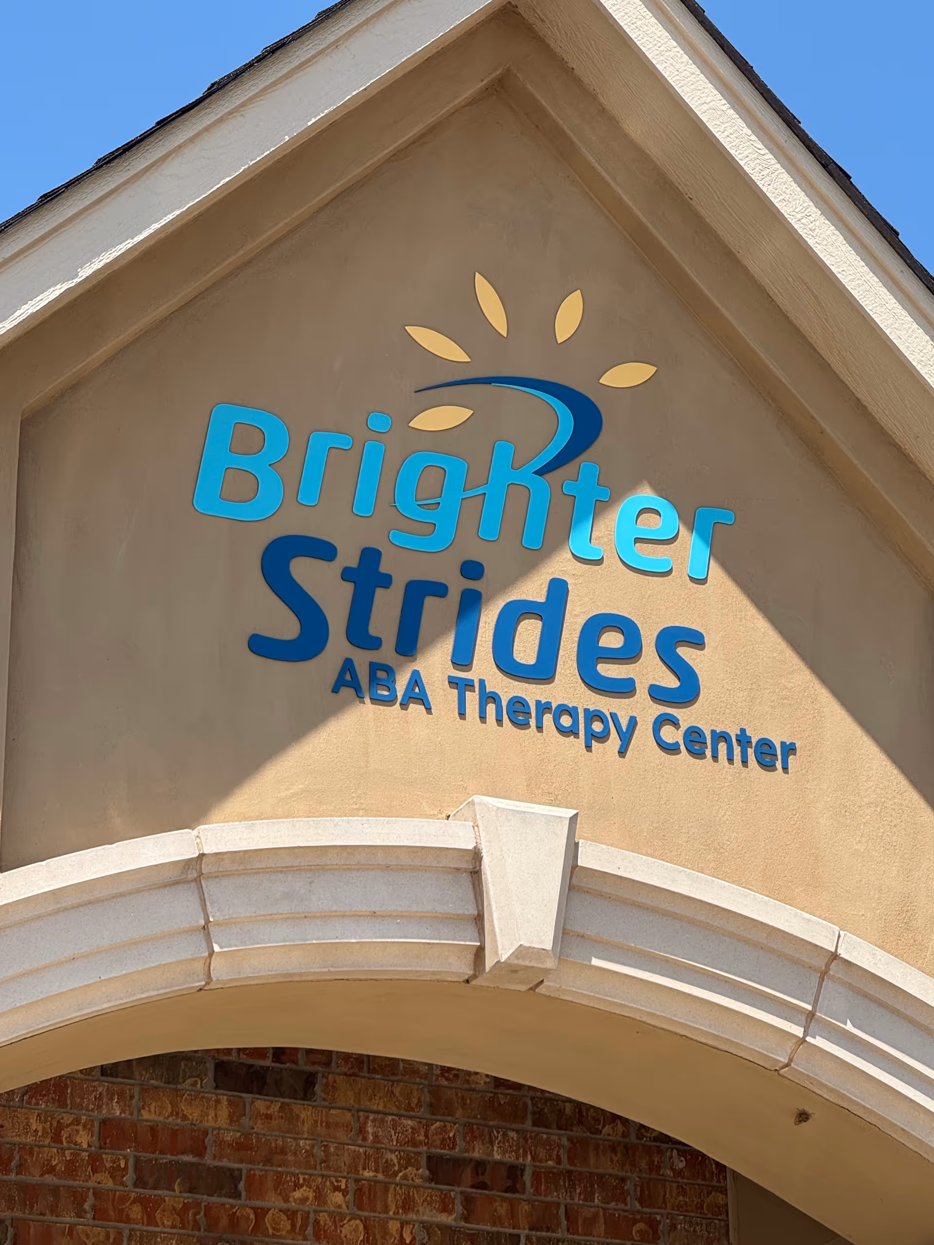 Exterior wall signage for Brighter Strides ABA Therapy Center against a blue sky.