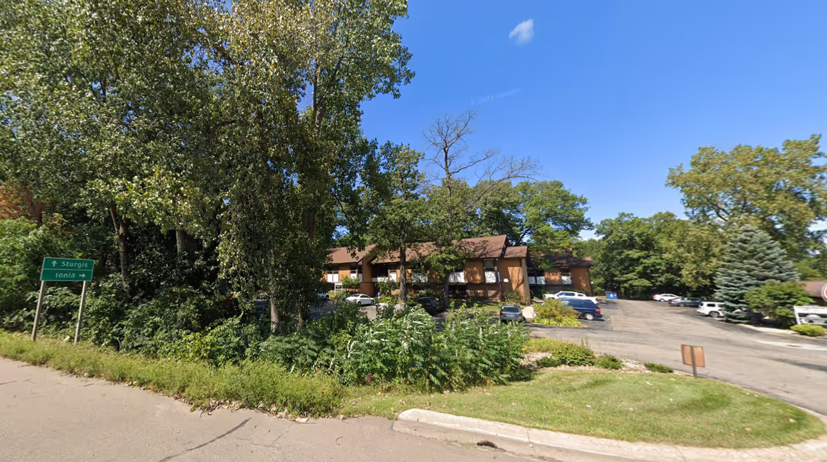 Exterior view of a brick senior care facility with parking and mature trees
