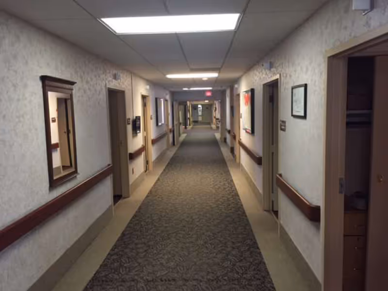 Long hallway inside Parma Care Center with doors, railings, and patterned carpet.