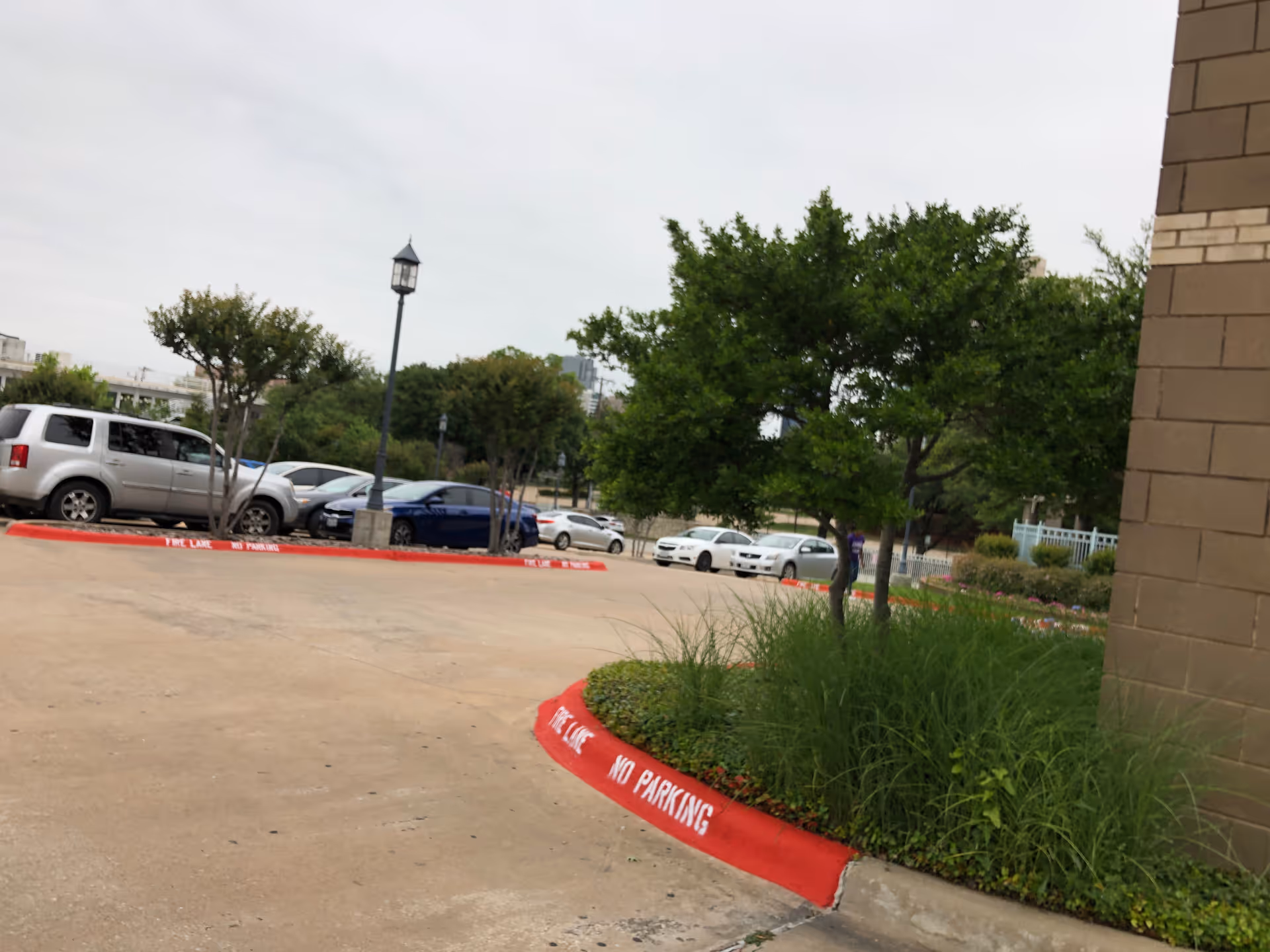Parking lot with several cars, landscaping, and a brick building facade.