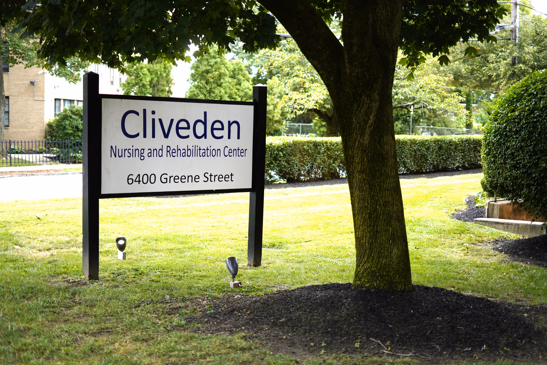 Exterior view of Cliveden Nursing and Rehabilitation Center sign beside a tree and hedges.