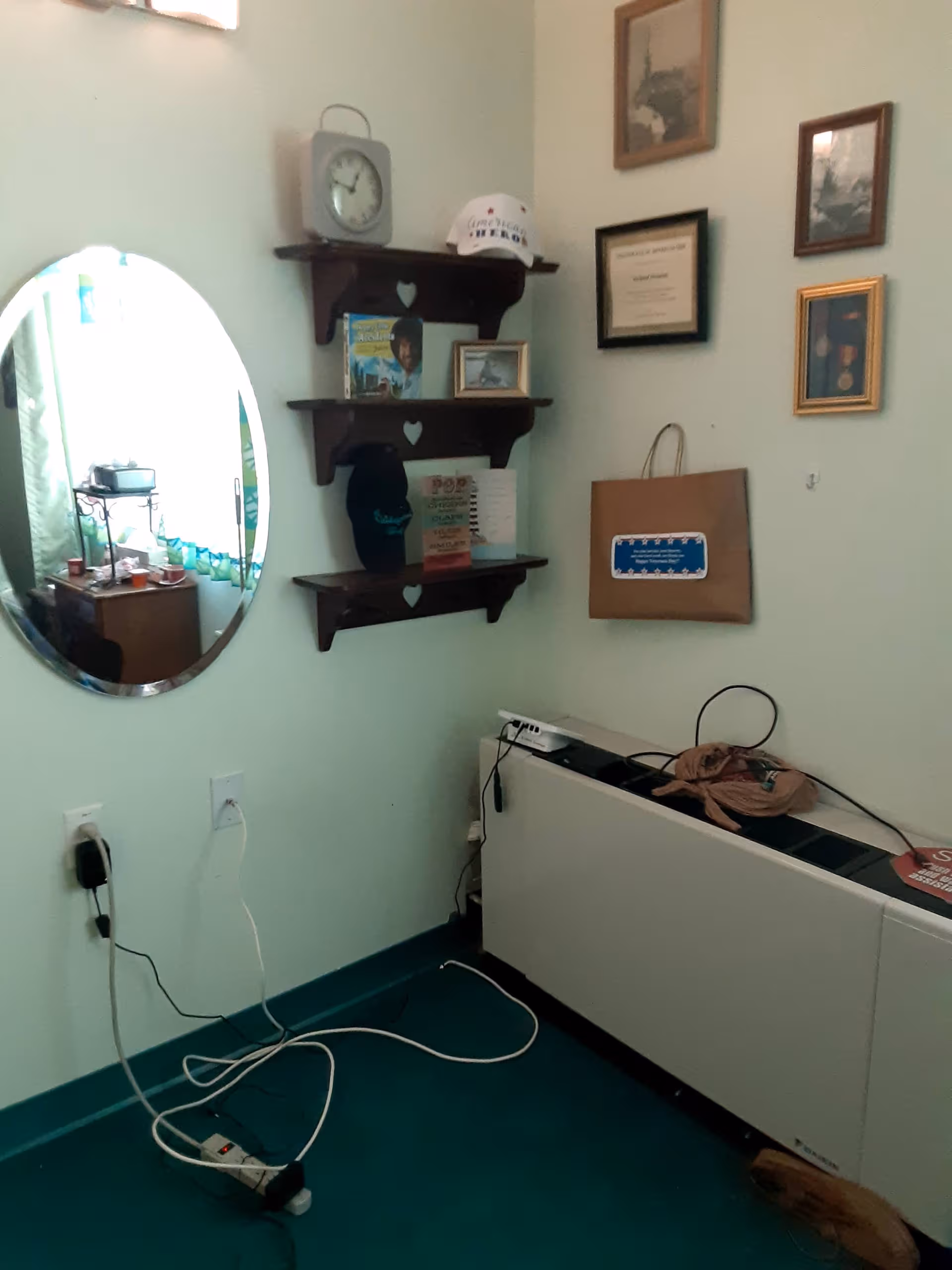 Oval mirror beside shelves with framed photos, cords, and a beige cabinet in a small interior.