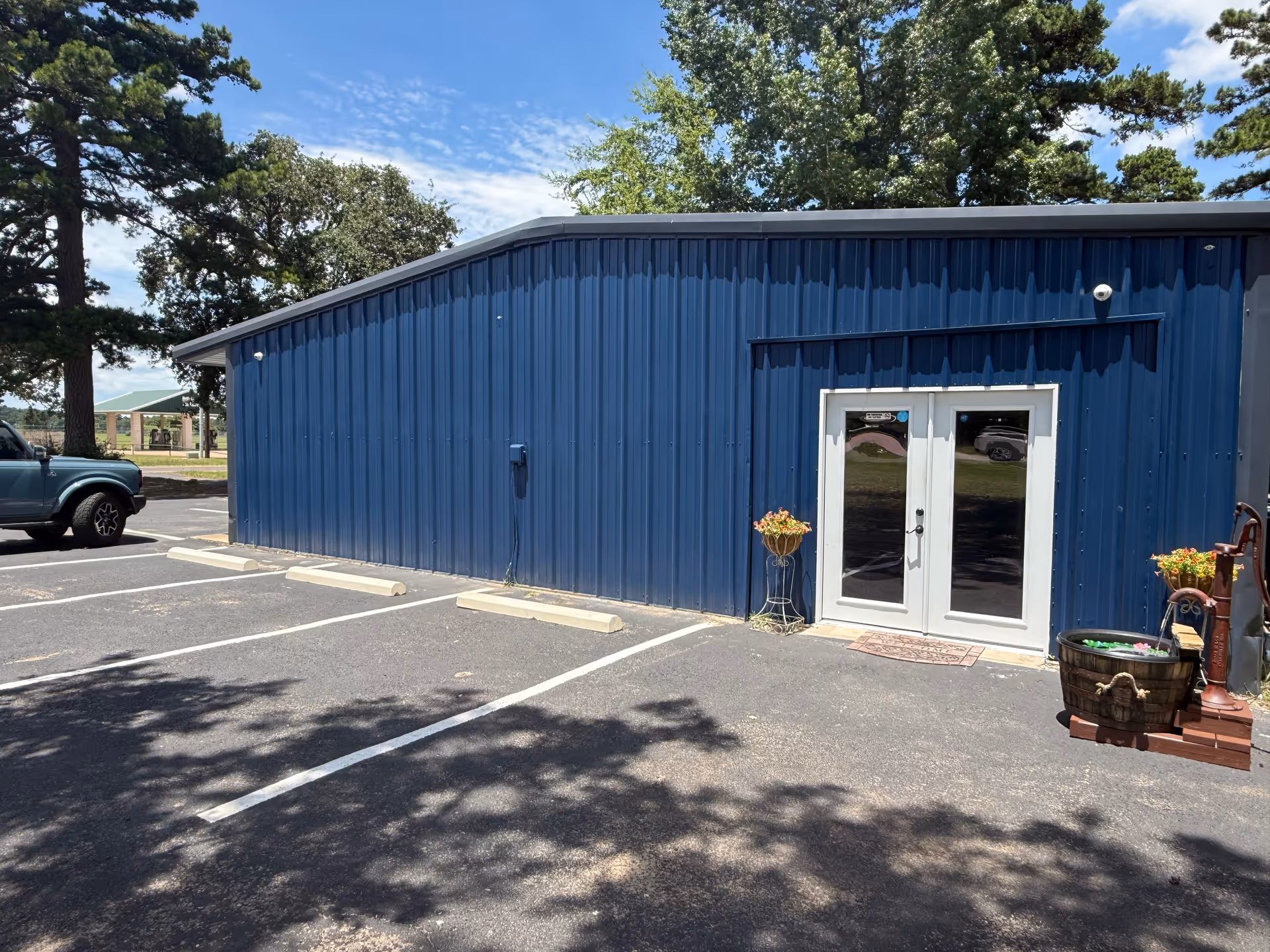 Blue metal building exterior with double glass doors, parking spaces, and potted plants.