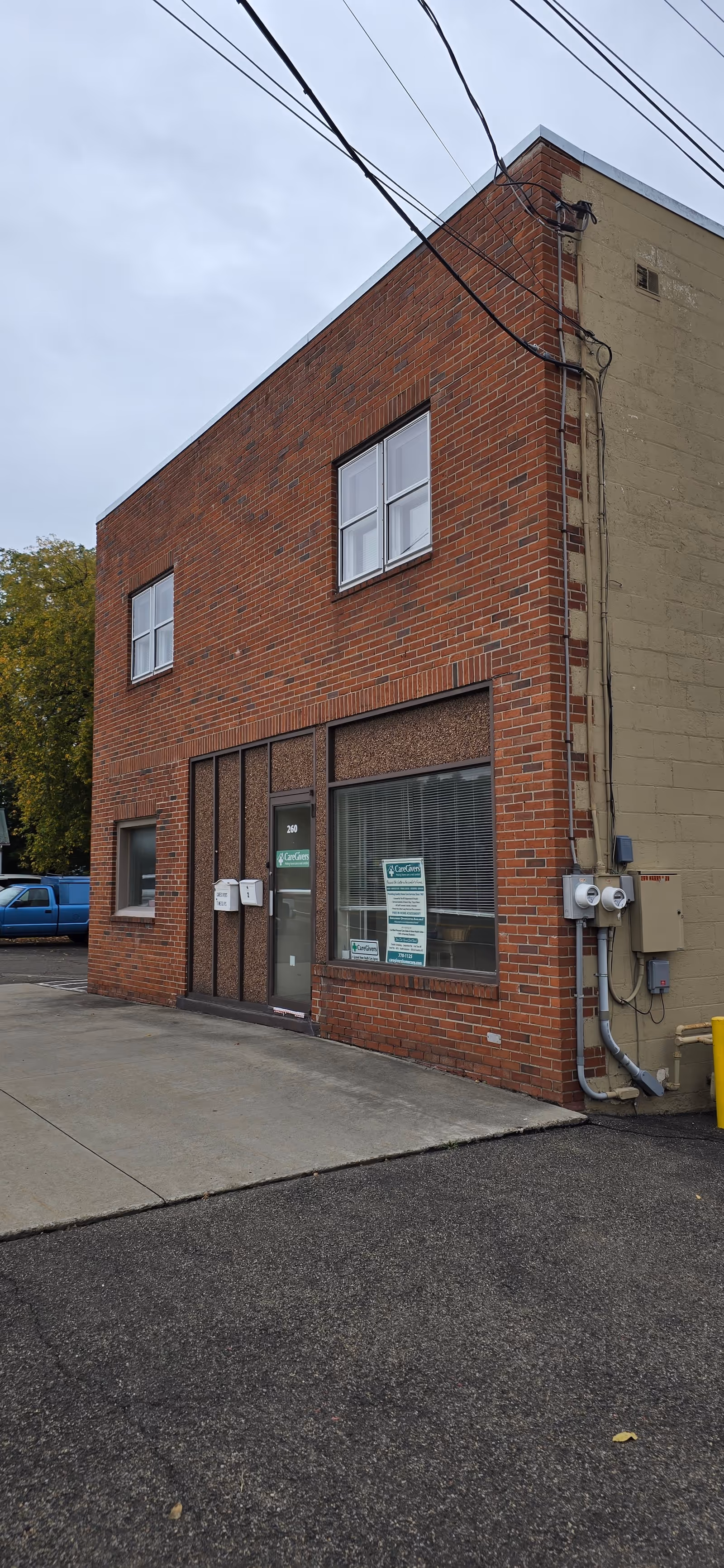 Brick two-story building exterior with glass door, large windows, and side utility meters.