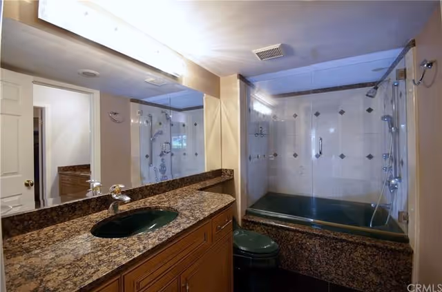 Modern bathroom in senior living facility with granite counter, sink, and glass-enclosed shower.