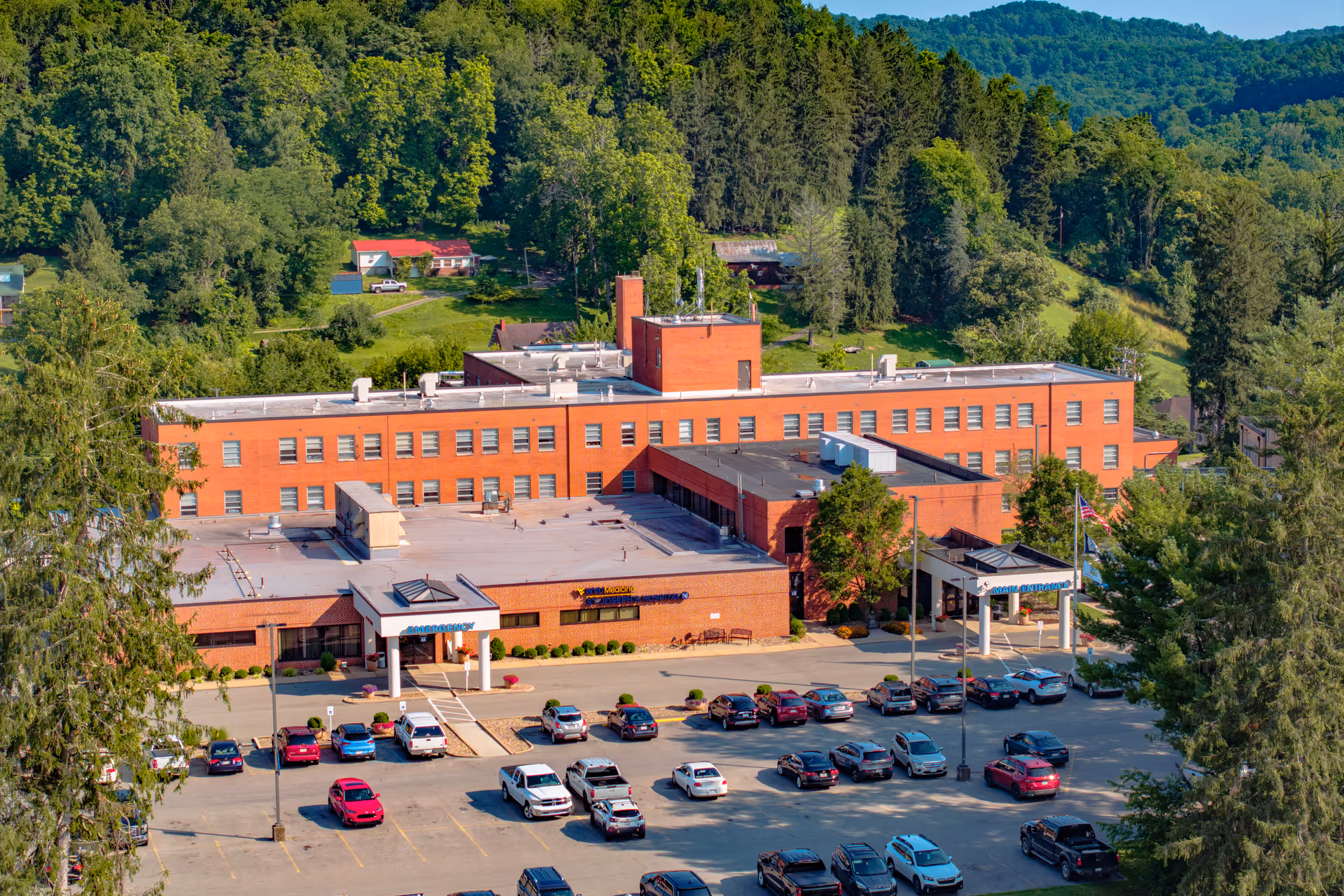 Aerial view of a red brick hospital building with a parking lot and surrounding trees