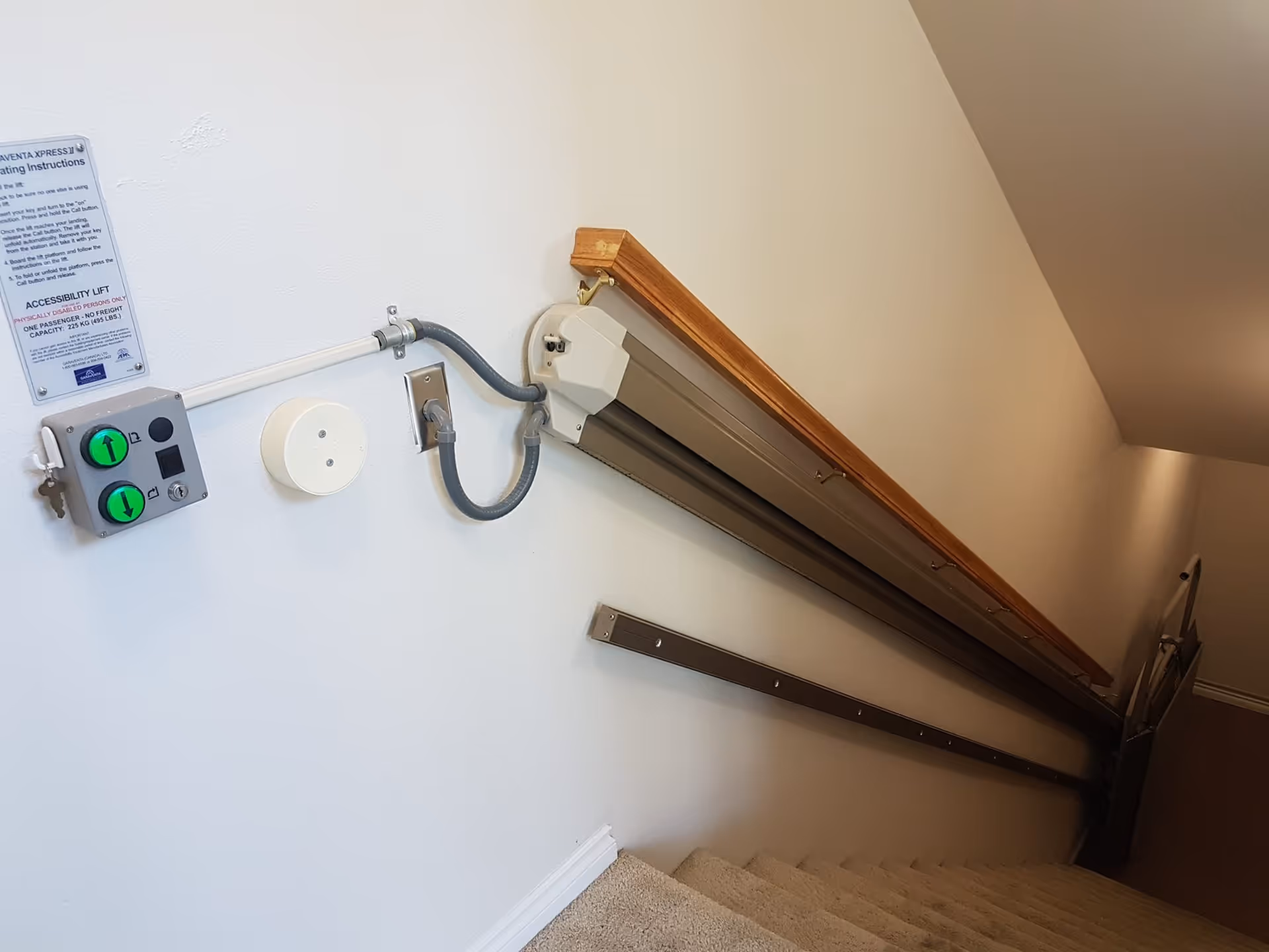 Indoor stair lift along a stairwell with wall-mounted control panel and wooden handrail.