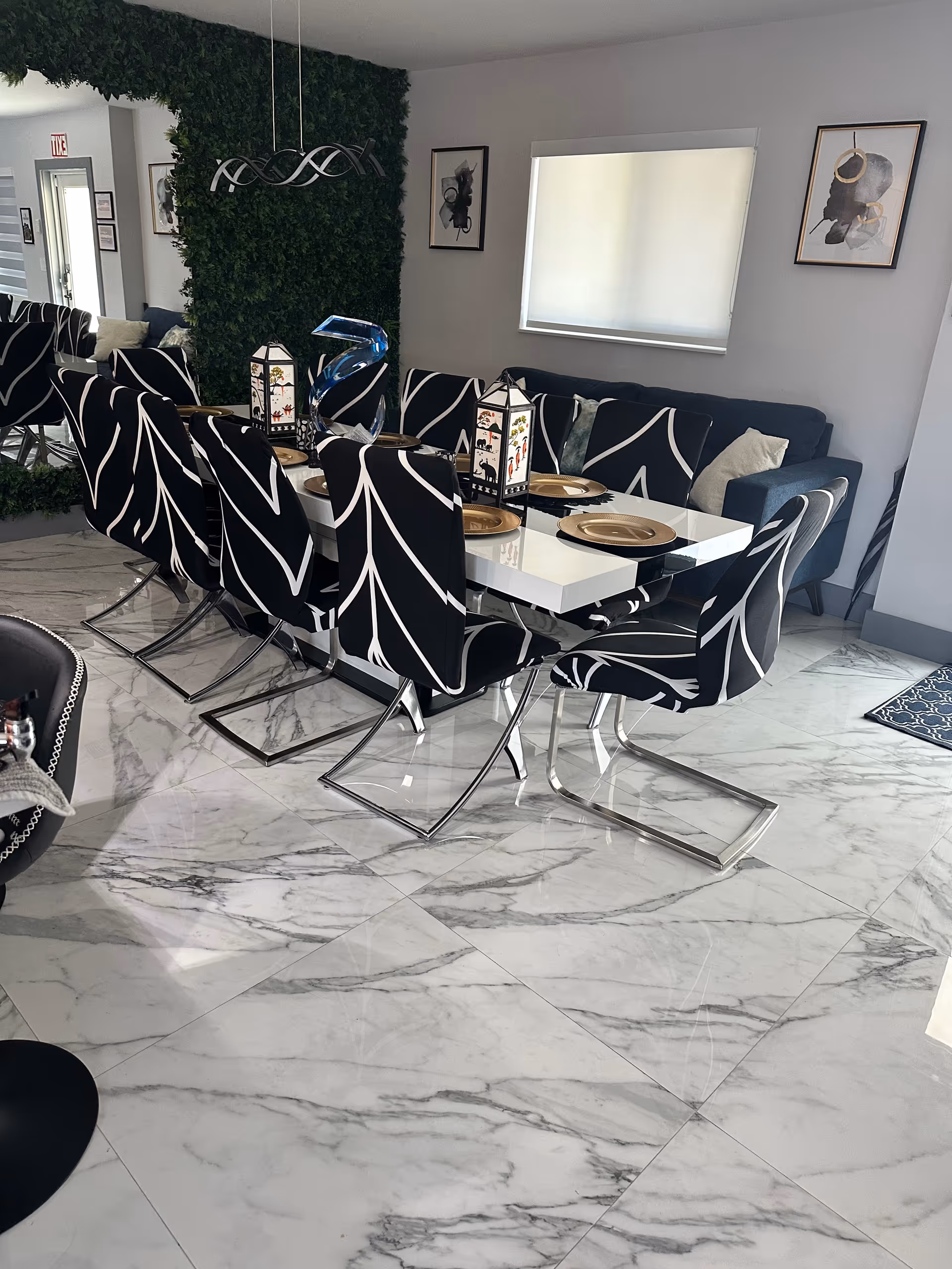 A modern dining room with a long white table, black patterned chairs, and lantern centerpieces.