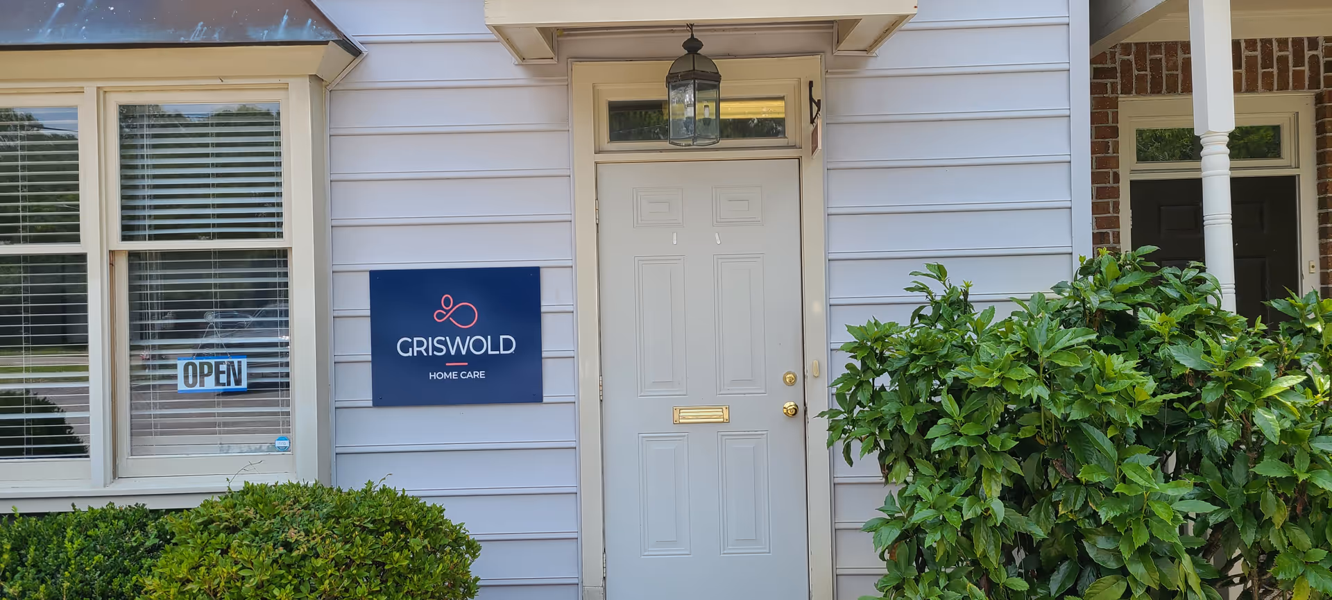 Front entrance of Griswold Home Care building with sign, door, window, and greenery.
