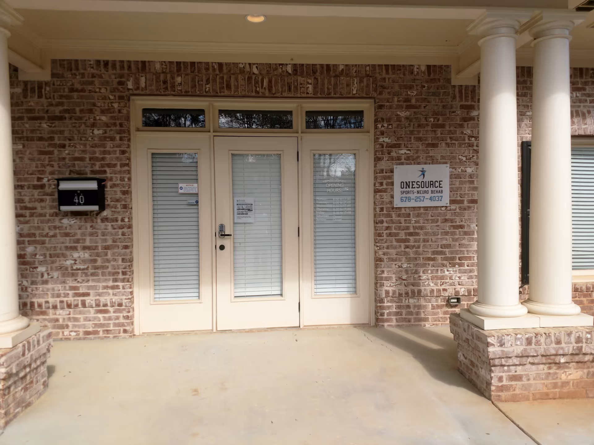 Brick building exterior with double doors, white columns, and a sign reading Onesource Sports Neuro Rehab.