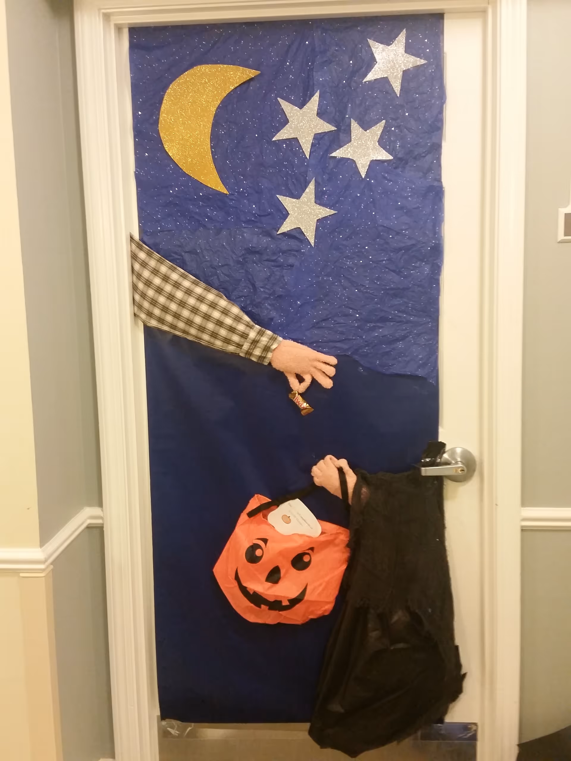 Door decorated for Halloween with stars; an arm hands a small item by a pumpkin bag.