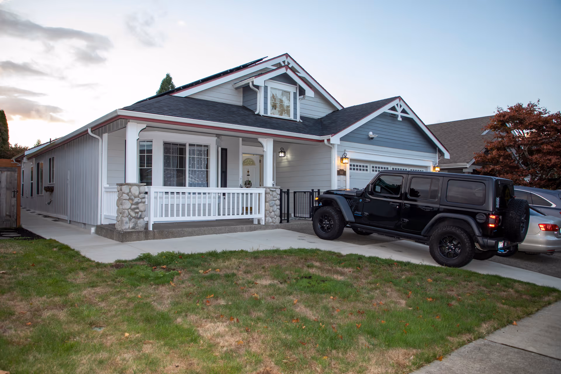 Single-story home with a front porch, stone pillars, and a black Jeep in the driveway.
