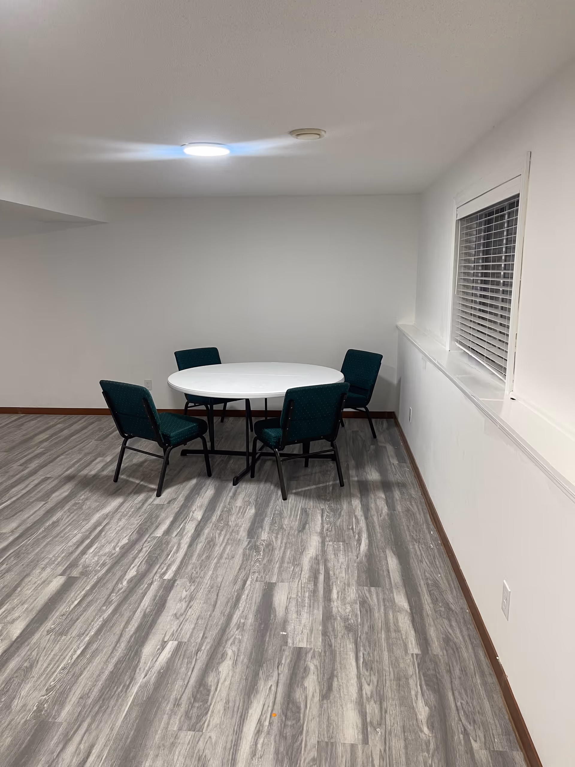Empty dining area with round white table and four green chairs in a small room.