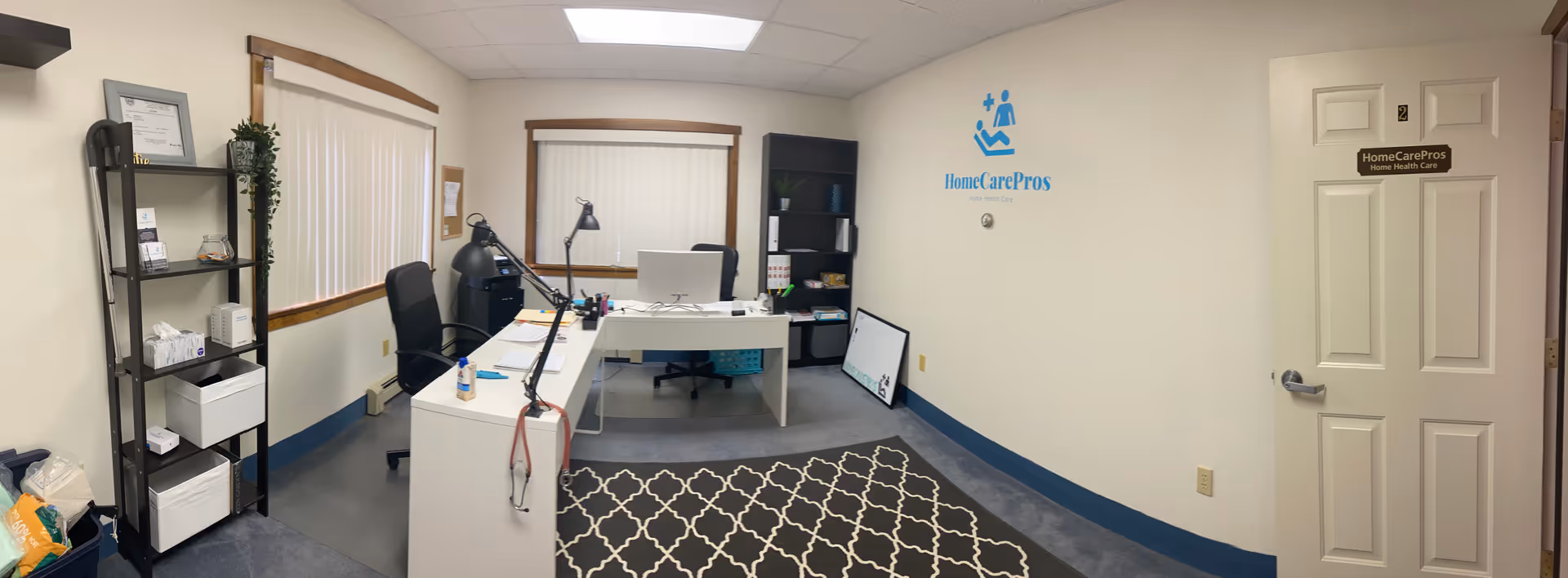 Office reception area inside a HomeCarePros facility with desks, computer, and shelving.