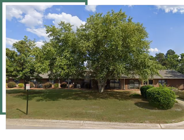 Front exterior of a brick senior care center with trees and a grassy lawn.