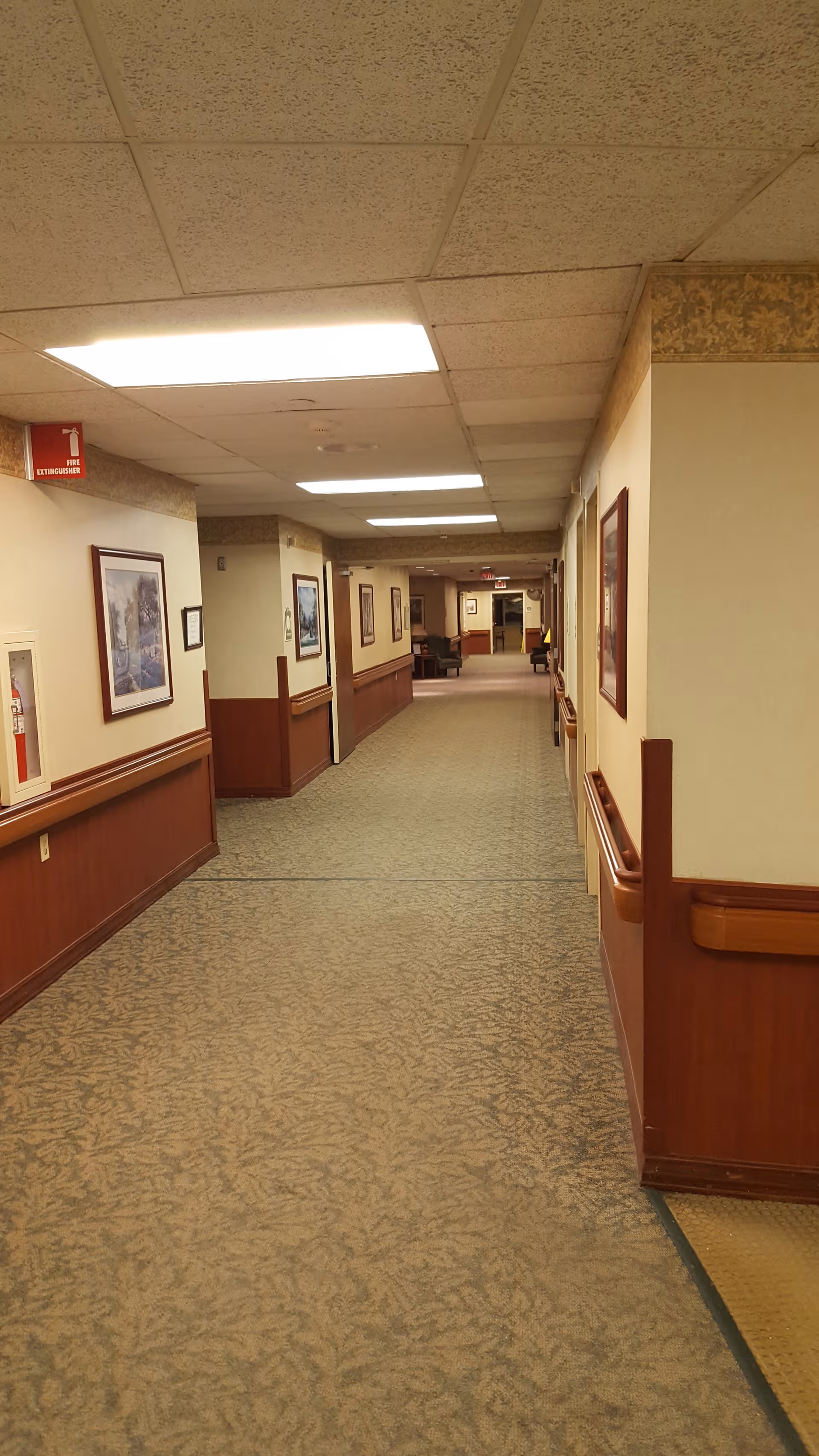 Long indoor hallway in a senior living facility with artwork along the walls.