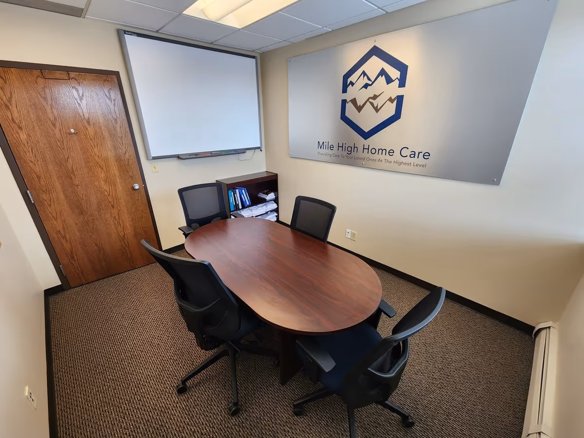 Small conference room with oval table, chairs, whiteboard, and Mile High Home Care logo on wall.