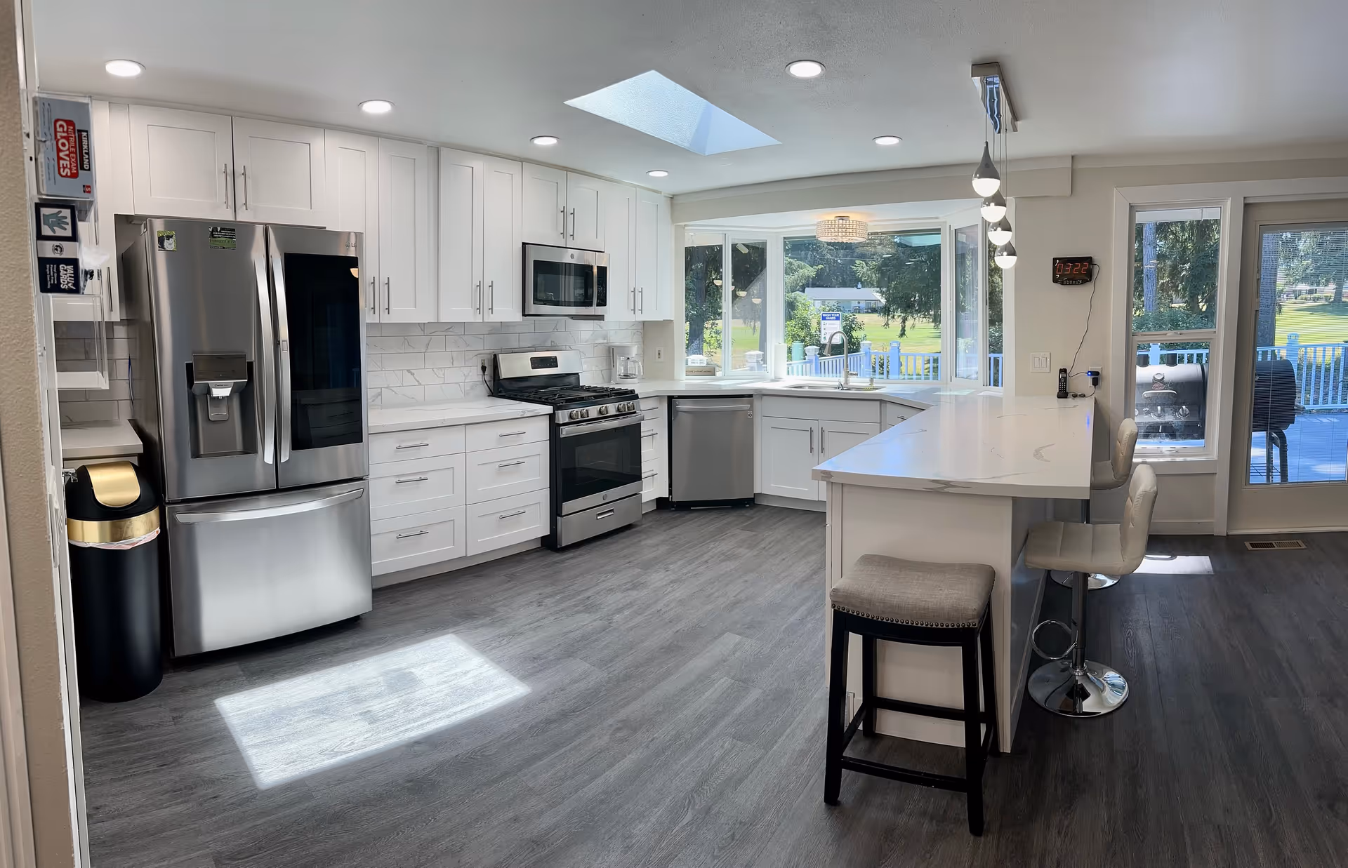 Bright, modern kitchen with white cabinets, stainless appliances, an island, and large windows.