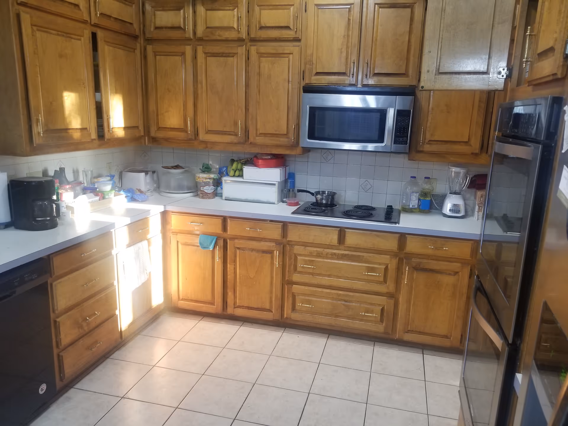 An L-shaped kitchen with wooden cabinets, a stove, microwave, toaster, and refrigerator.