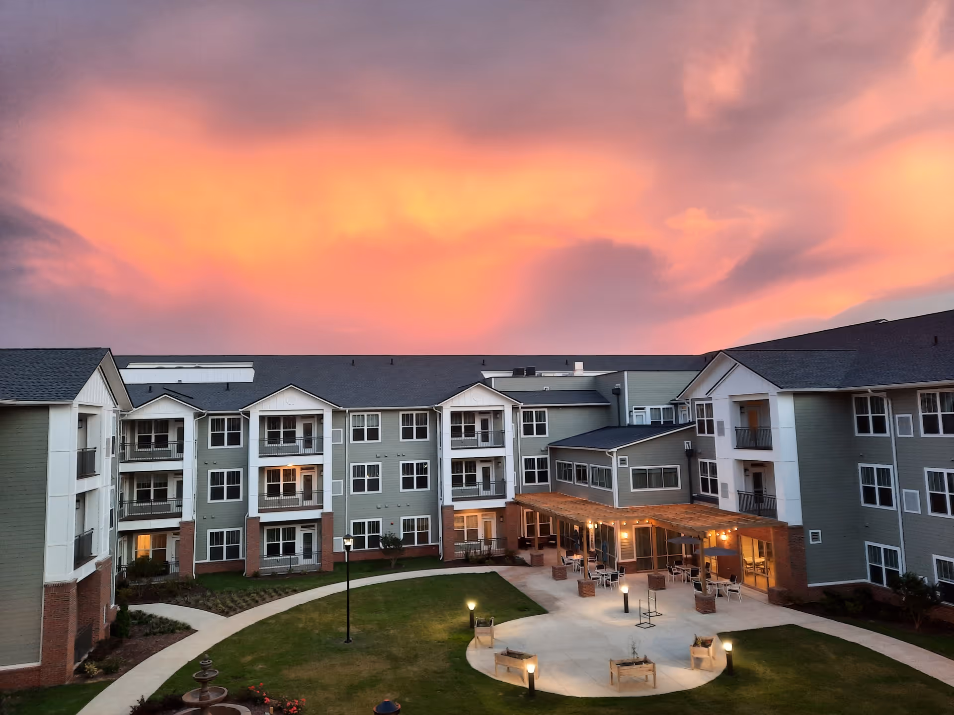 Courtyard and three-story senior living building under a glowing orange sunset sky.