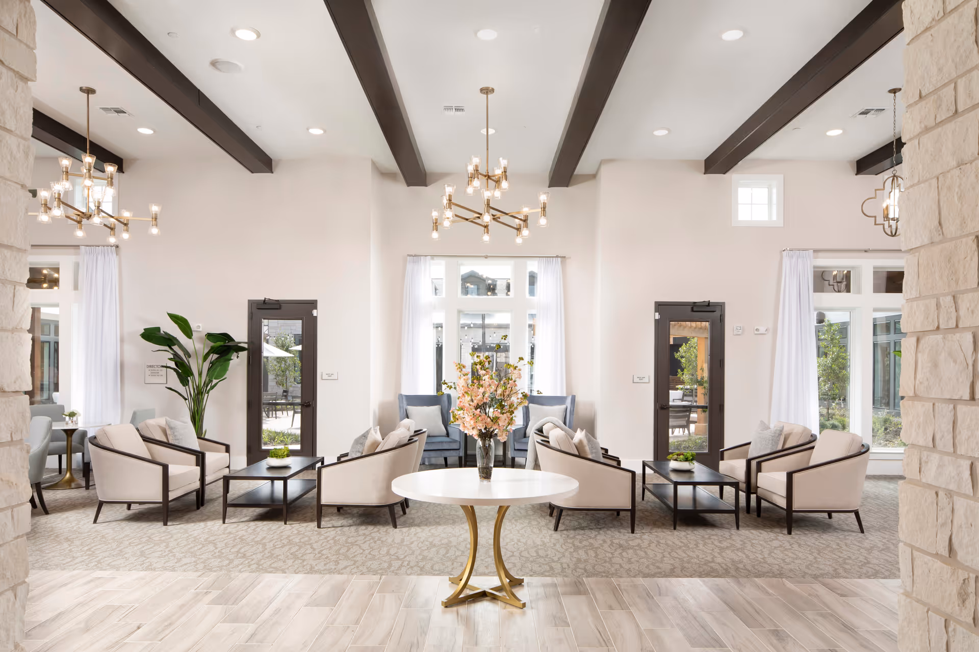 Bright senior living lounge with beige seating, a central round table, and large windows.