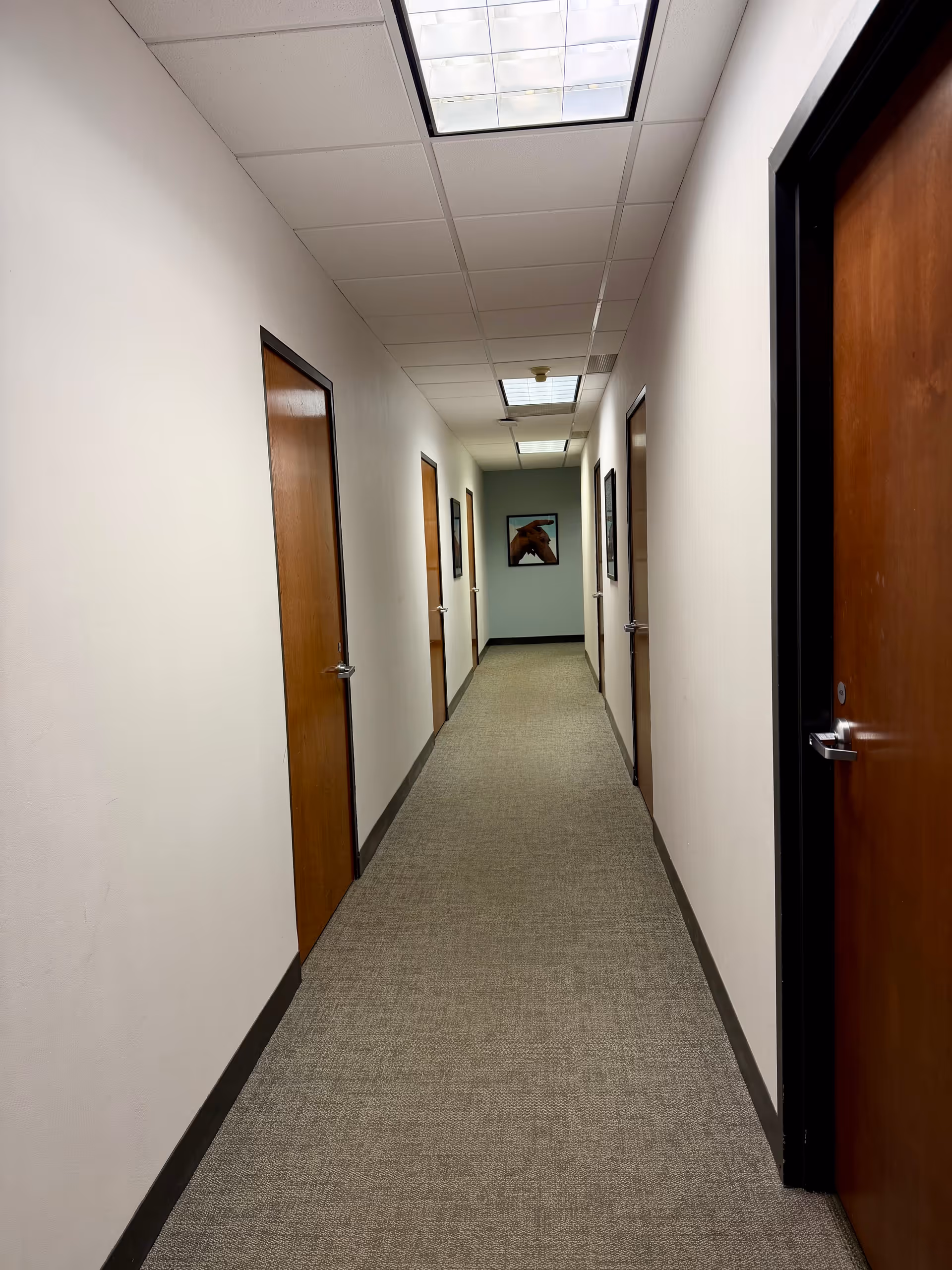 A long empty hallway with wooden doors and a drop ceiling in a senior facility.