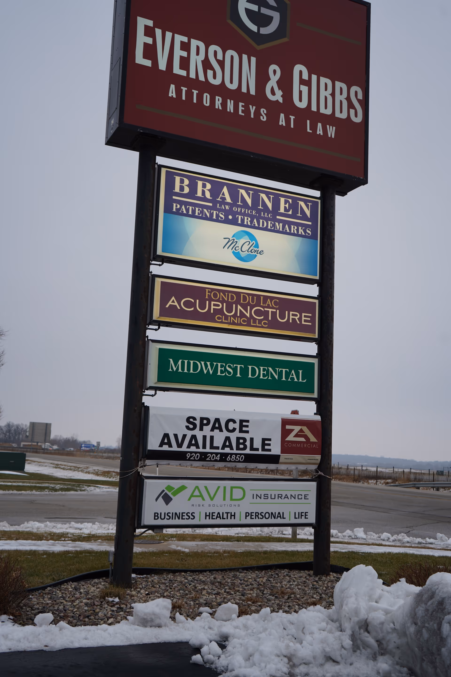 A tall outdoor signpost displays multiple business ads against a snowy background.