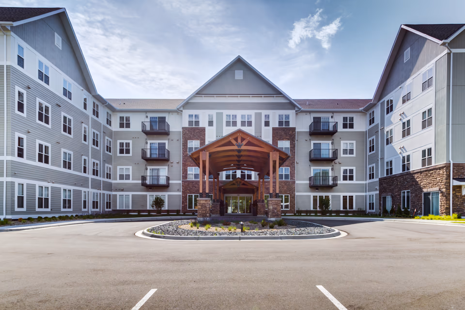 Front exterior view of Talamore Senior Living St. Cloud building with a covered entrance, multiple windows, balconies, and a circular driveway with landscaped center.
