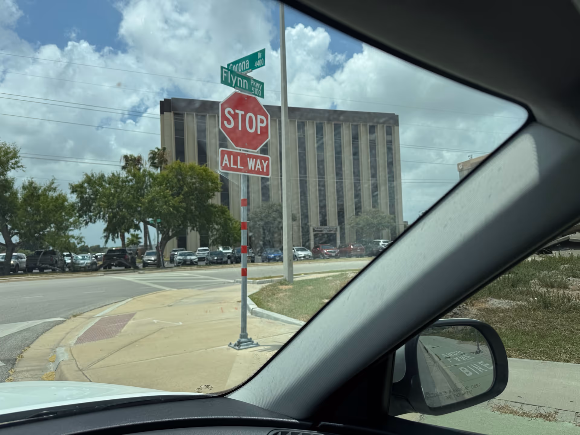 View from car window of a stop sign, street intersection, and a tall building ahead.