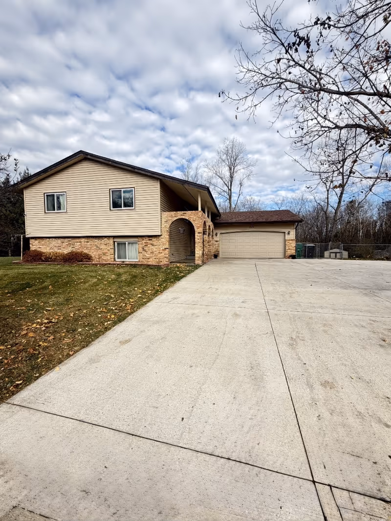 Two-story beige assisted-living building with brick accents, arched entry, attached garage, and driveway.
