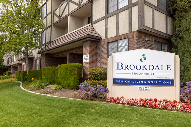 Front exterior of Brookdale Brookhurst senior living with sign and landscaped lawn.