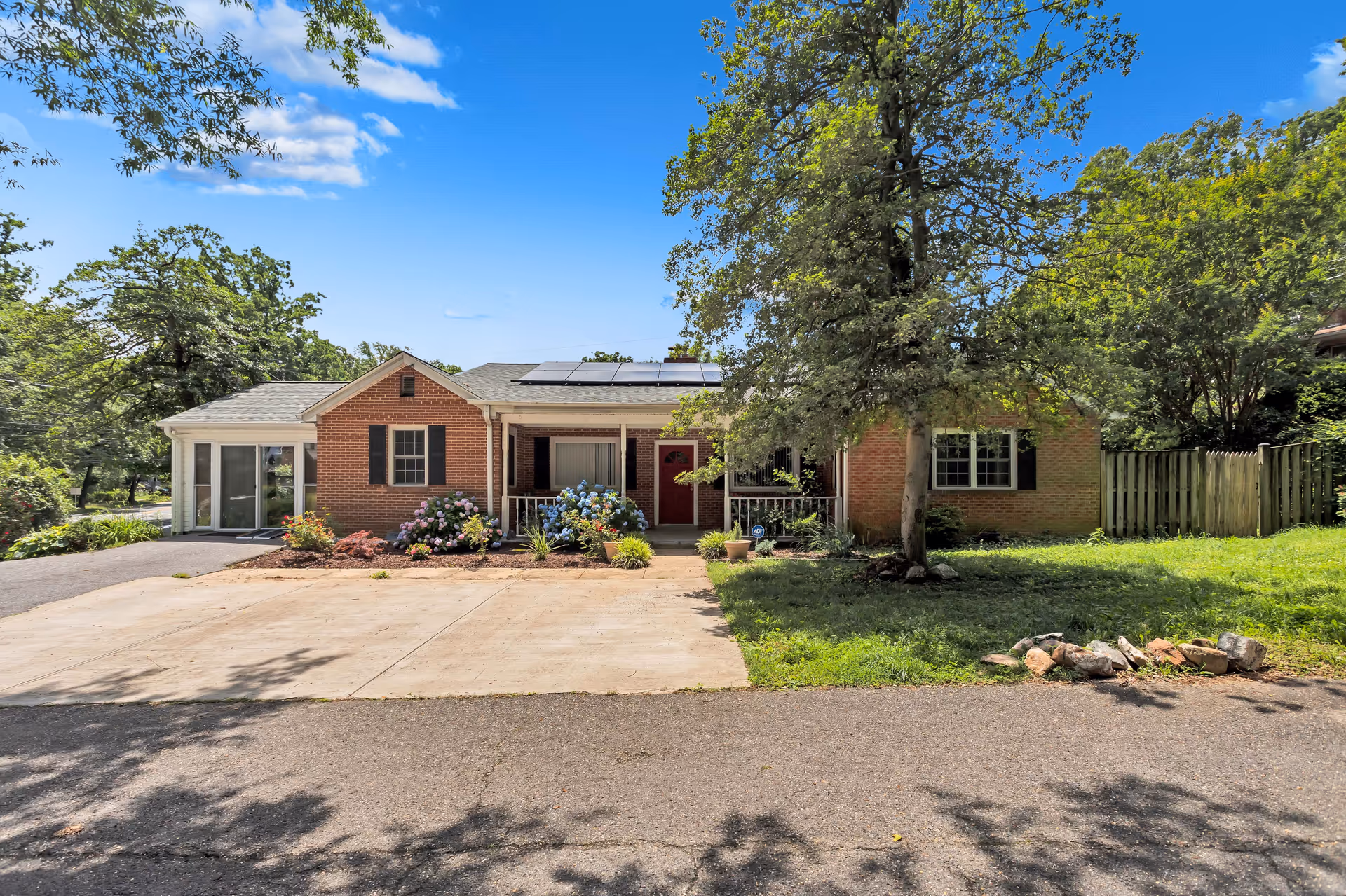 Brick, single-story house with a driveway, front porch, trees, and landscaped yard.