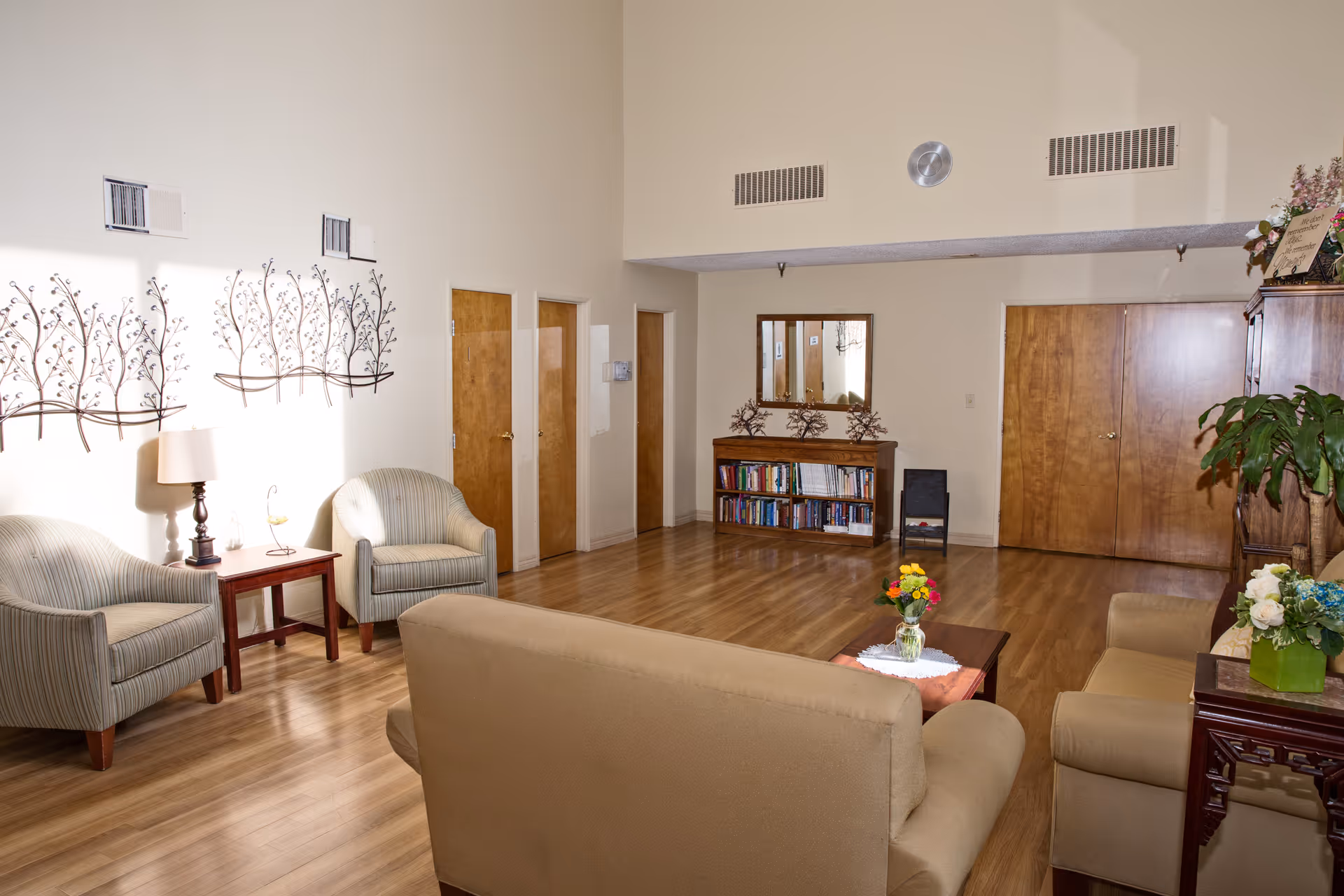 Senior living facility lounge with beige seating, wood floors, and a bookshelf.