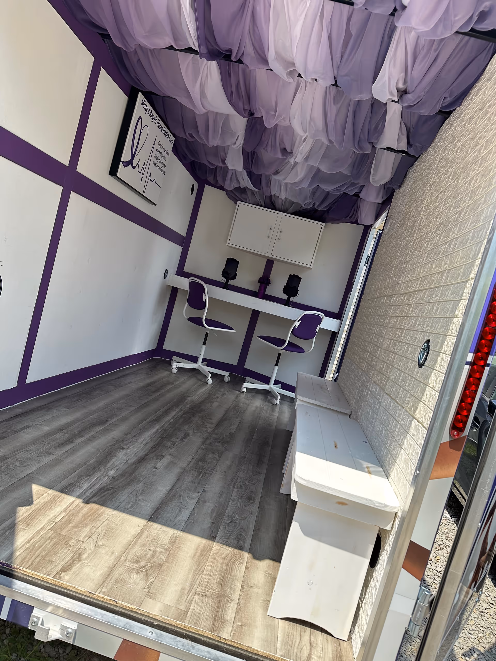 Purple-draped mobile interior with a long desk, two purple chairs, and cabinet.