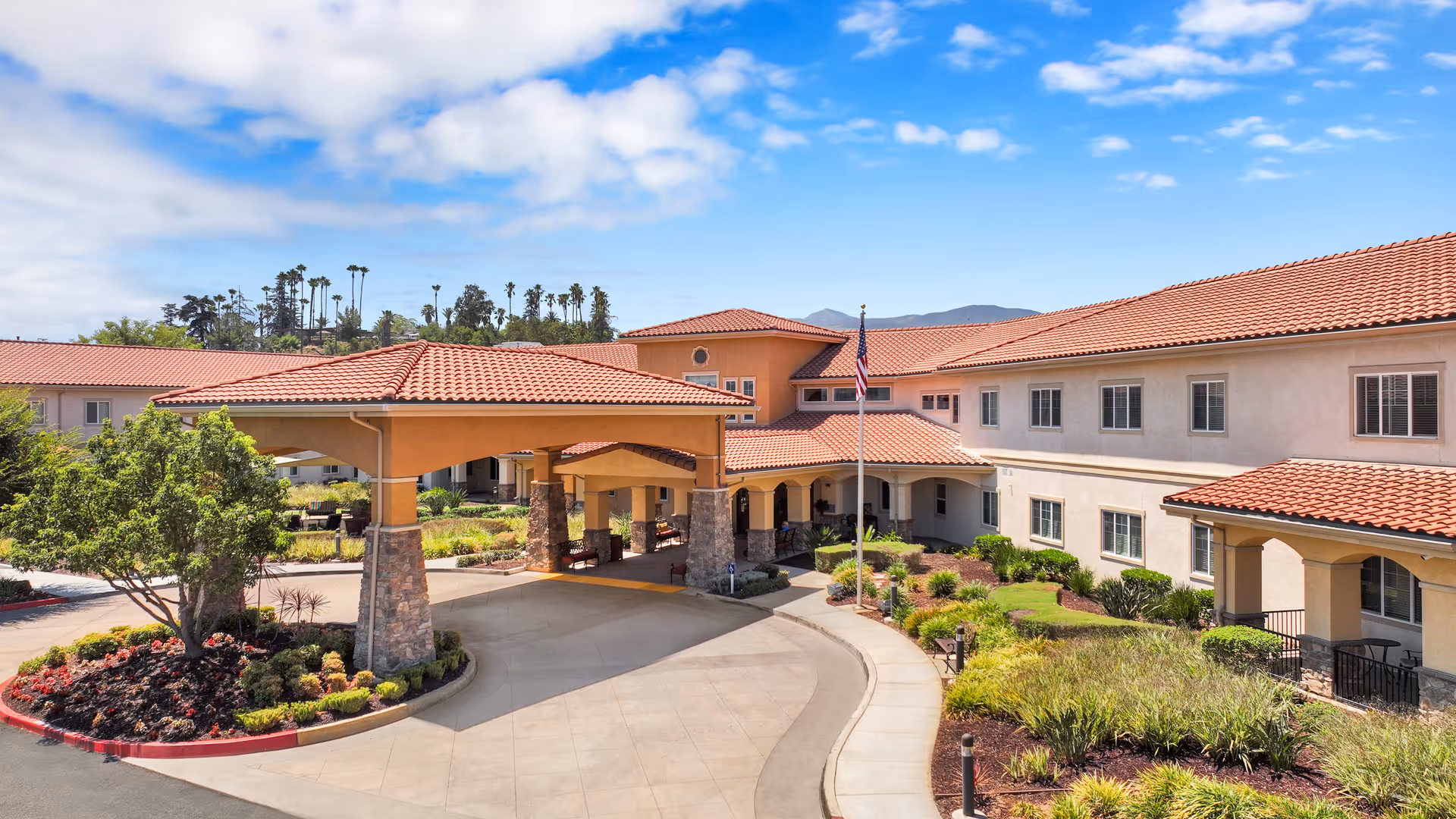 Exterior view of Estancia Del Sol with red-tiled roof, porte-cochere, and landscaped courtyard.