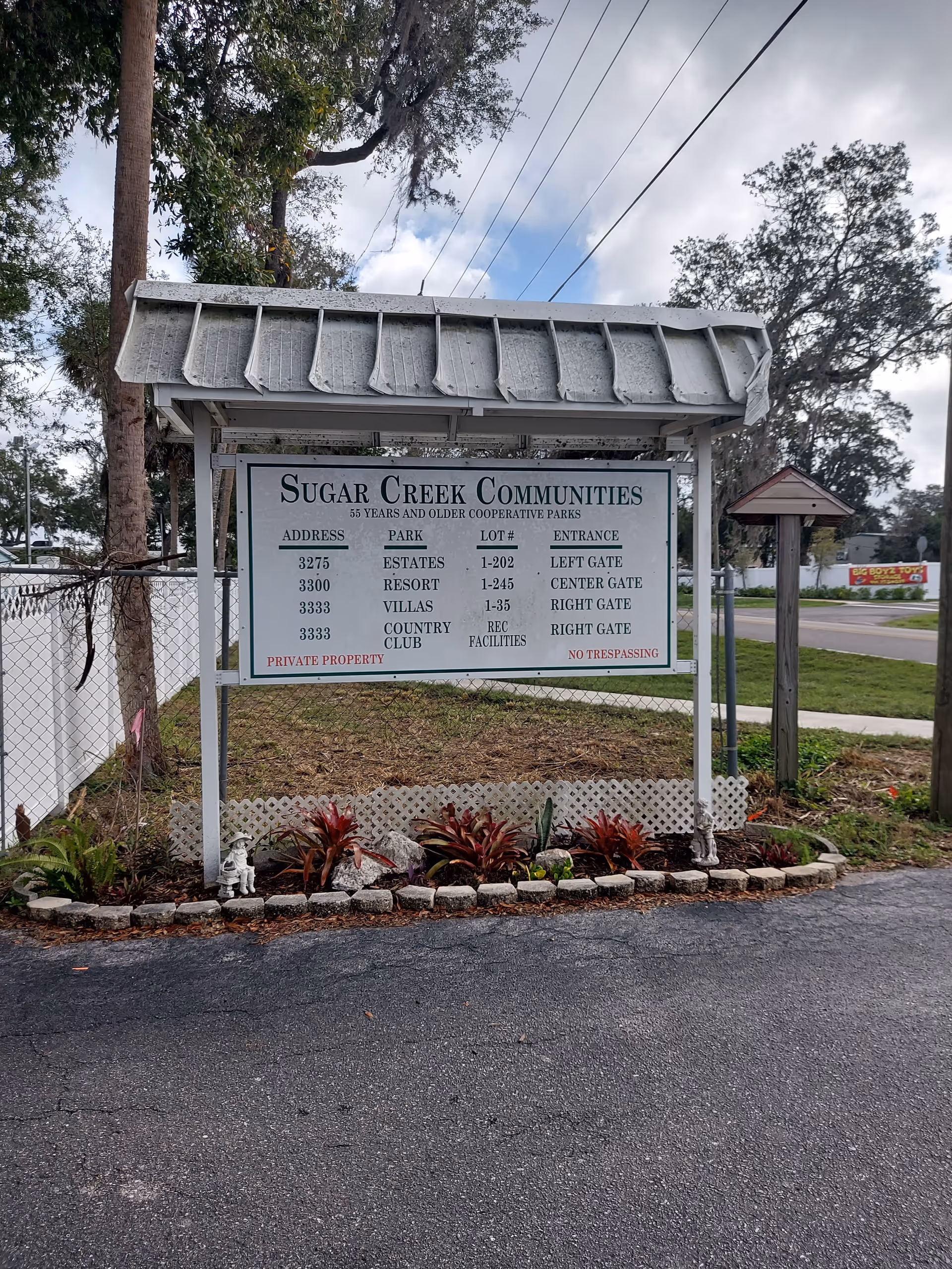 Front entrance sign for Sugar Creek Communities with landscaping and a paved road.