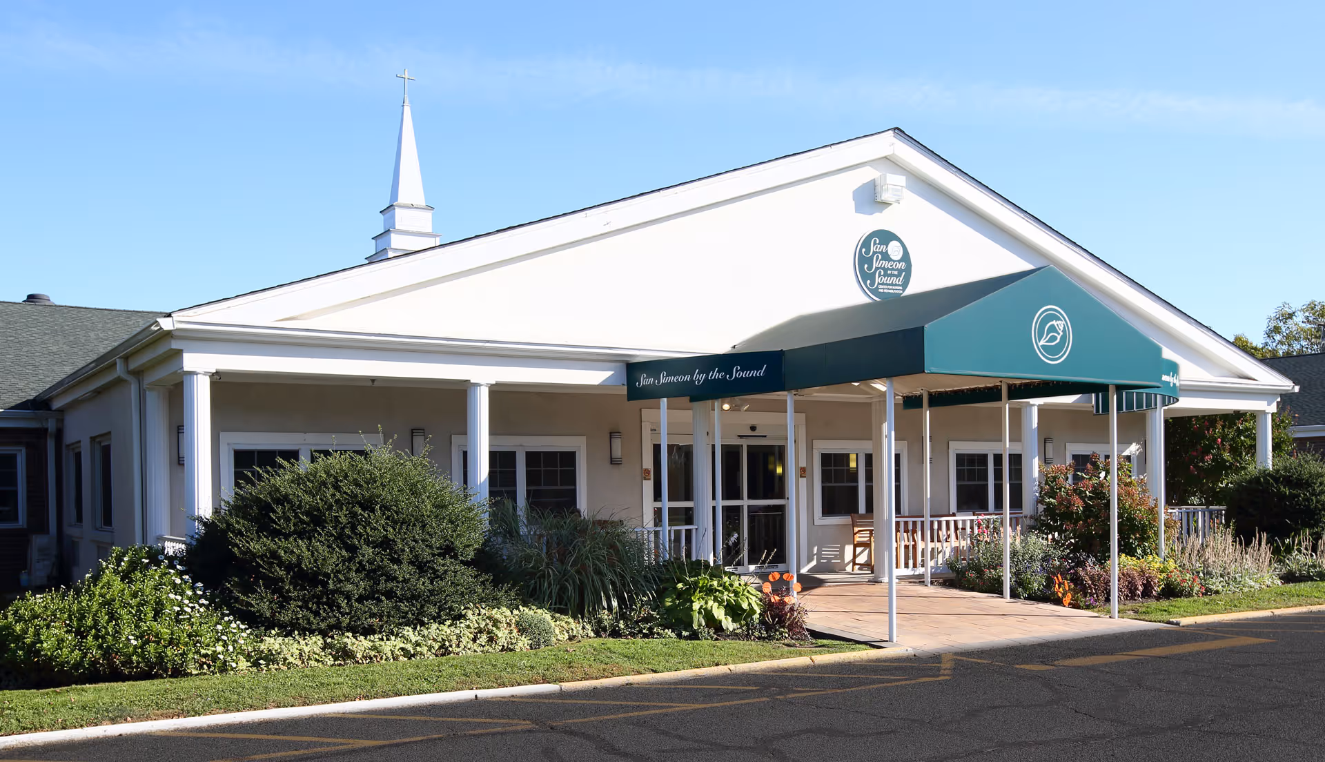 Single-story white building with teal awning, labeled San Simeon by the Sound.