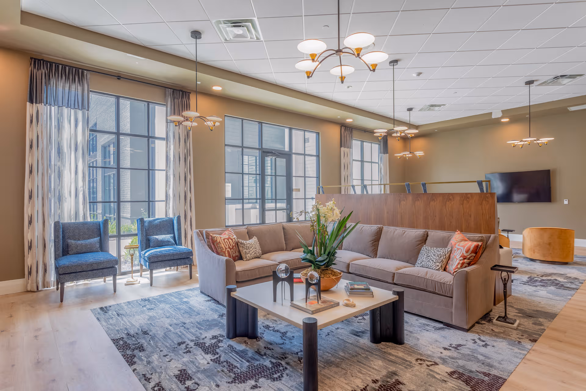 Bright senior-living lounge with sofa, chairs, coffee table, and large windows.