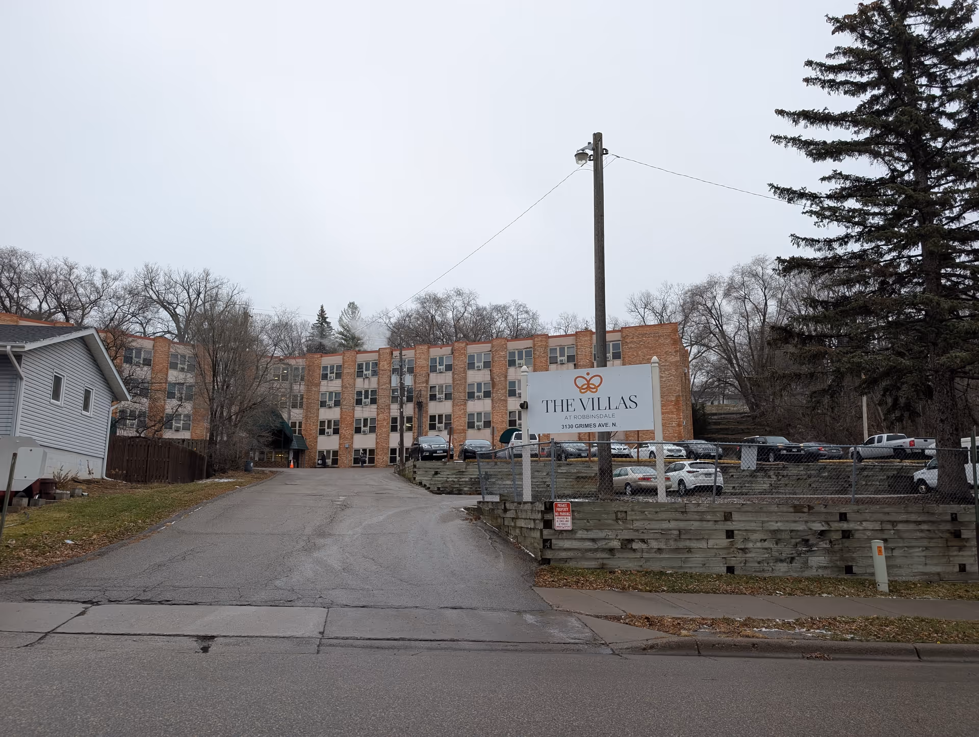 Front exterior of a multi-story brick senior living building with a driveway and a sign reading 'The Villas'.