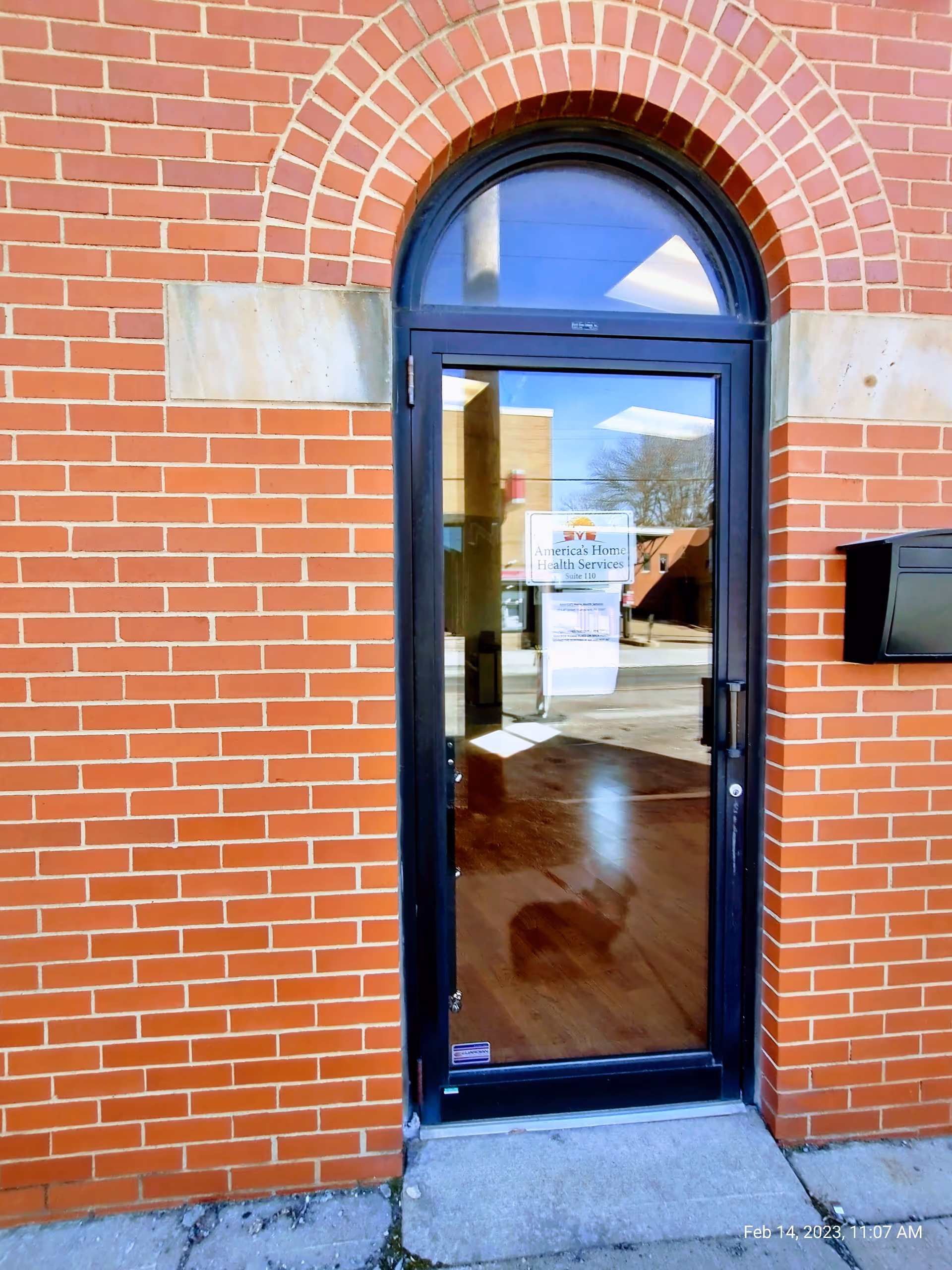 Brick building exterior with a glass front door, arched window, and America's Home Health Services sign.