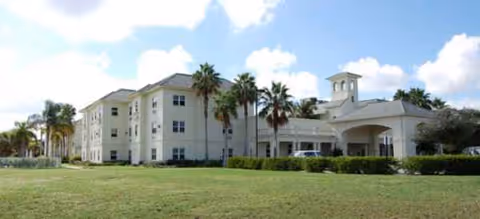 White senior living facility with palm trees and a covered front entrance.