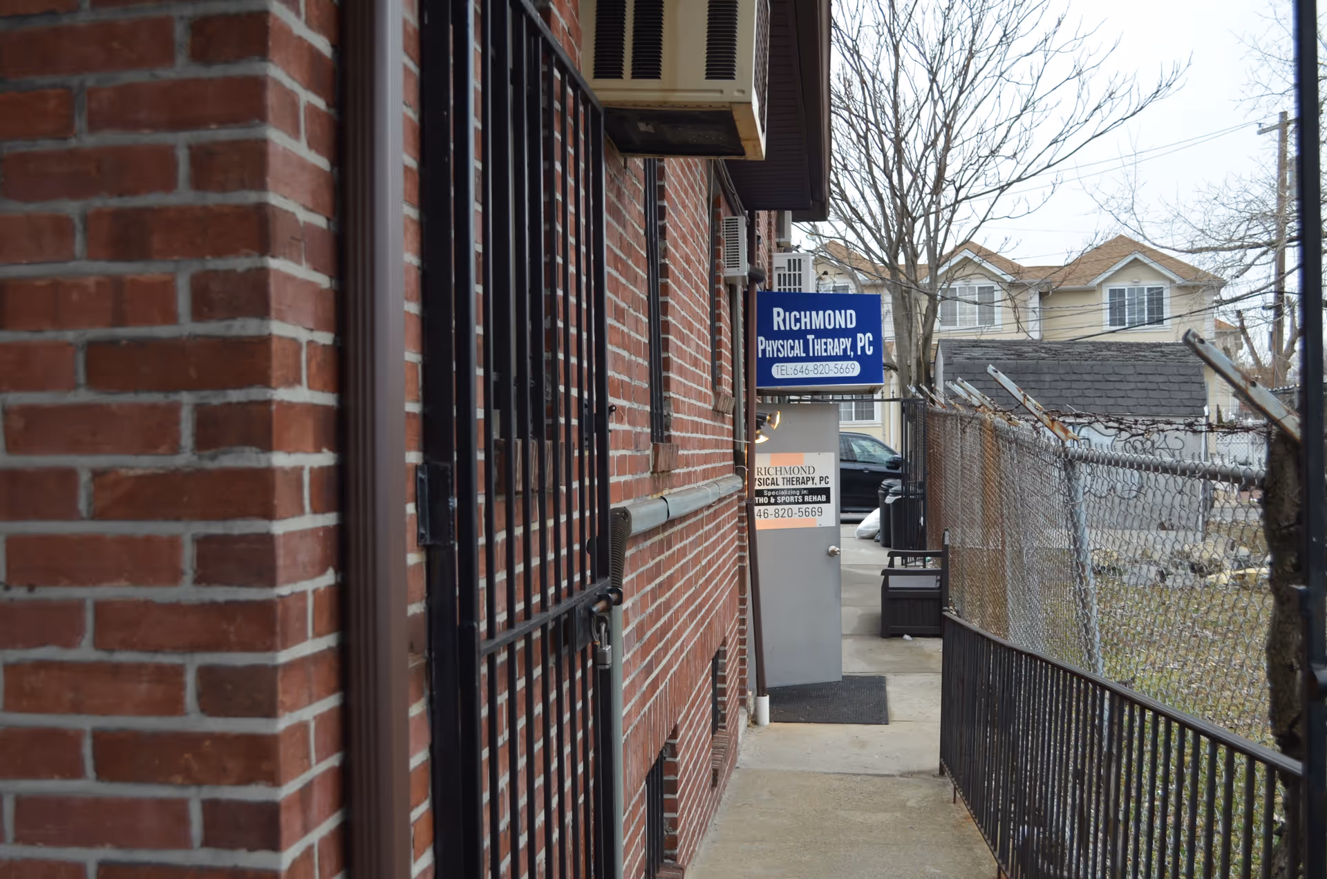 Brick exterior of Richmond Physical Therapy with blue sign along a narrow walkway