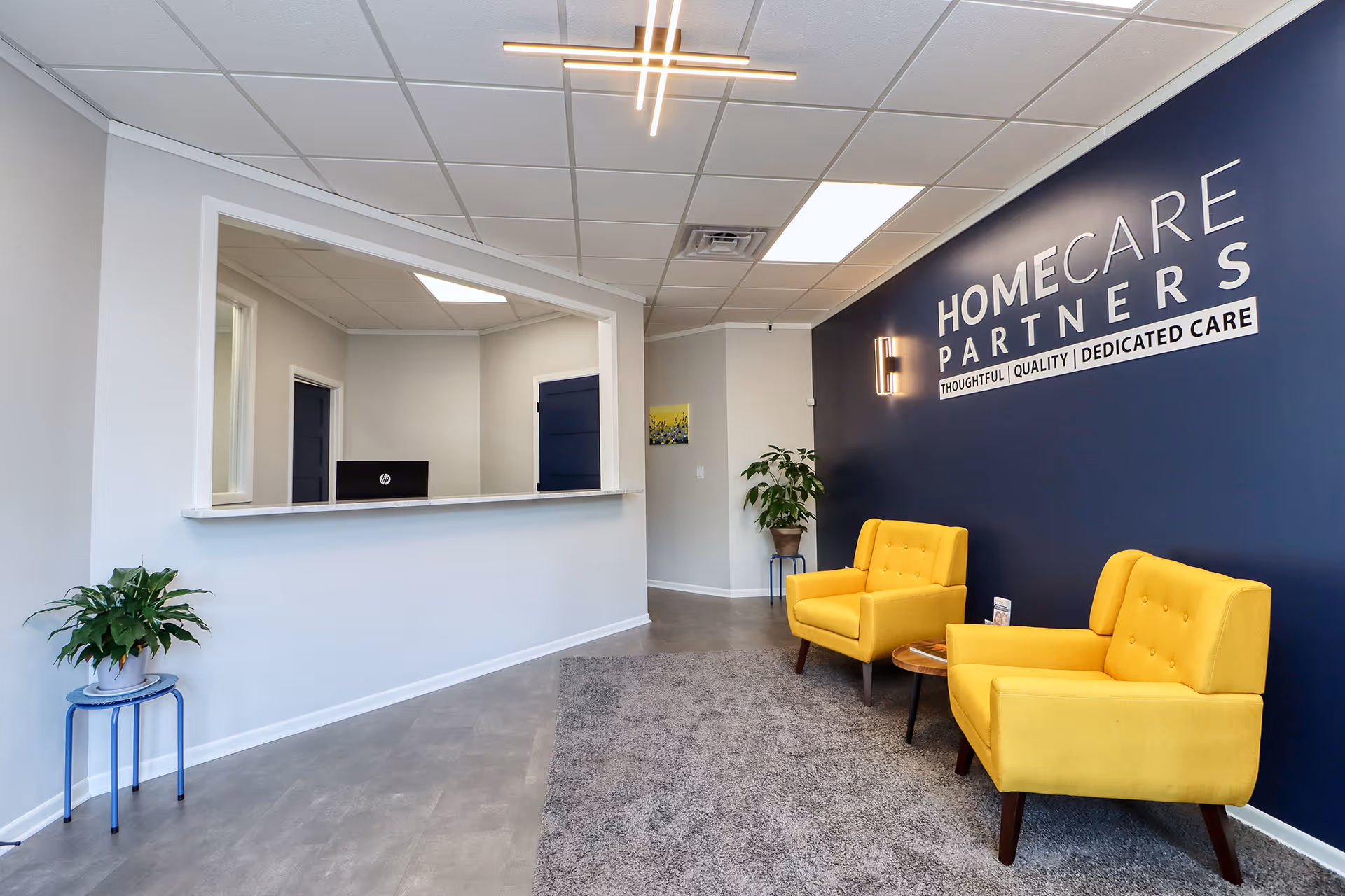 Reception area of Home Care Partners with navy wall, yellow chairs, and plants.
