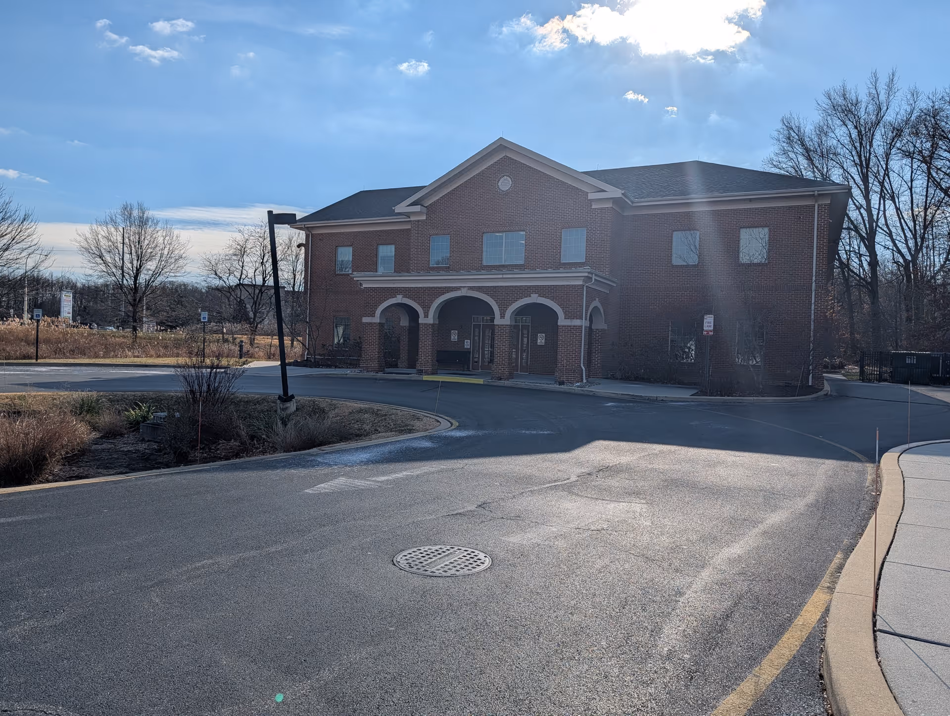 Two-story brick senior living facility with arched entry, circular drive, and leafless trees