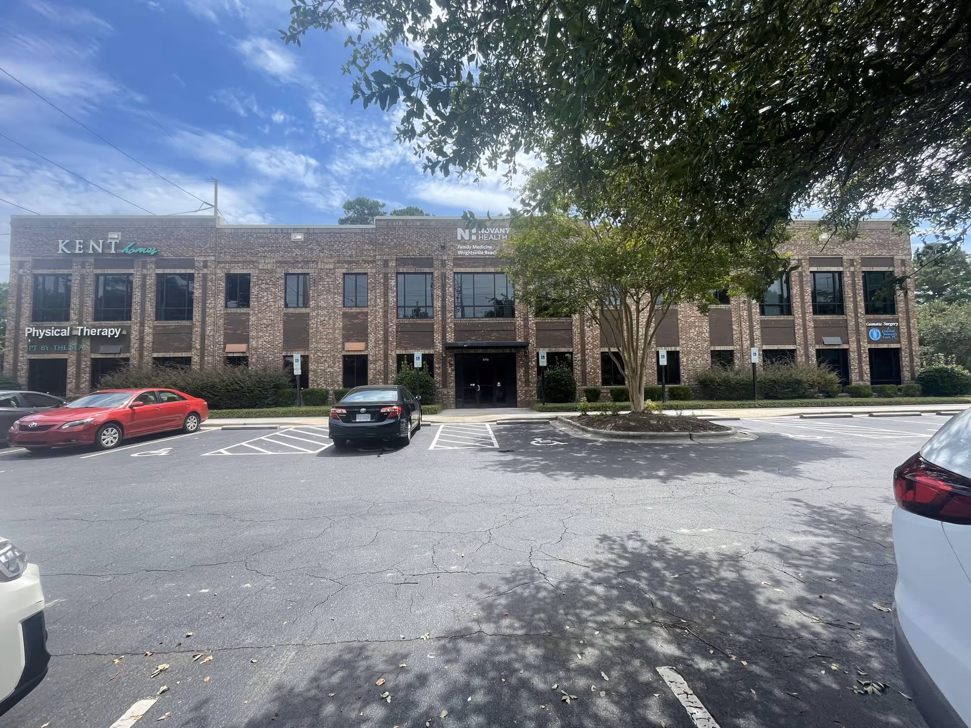 Brick senior living building facade with front entrance, parked cars, and trees.