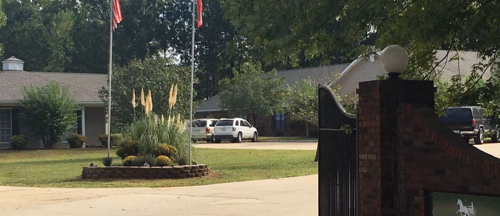 Gated entrance to Creekside Manor Assisted Living with a circular brick planter and flags.